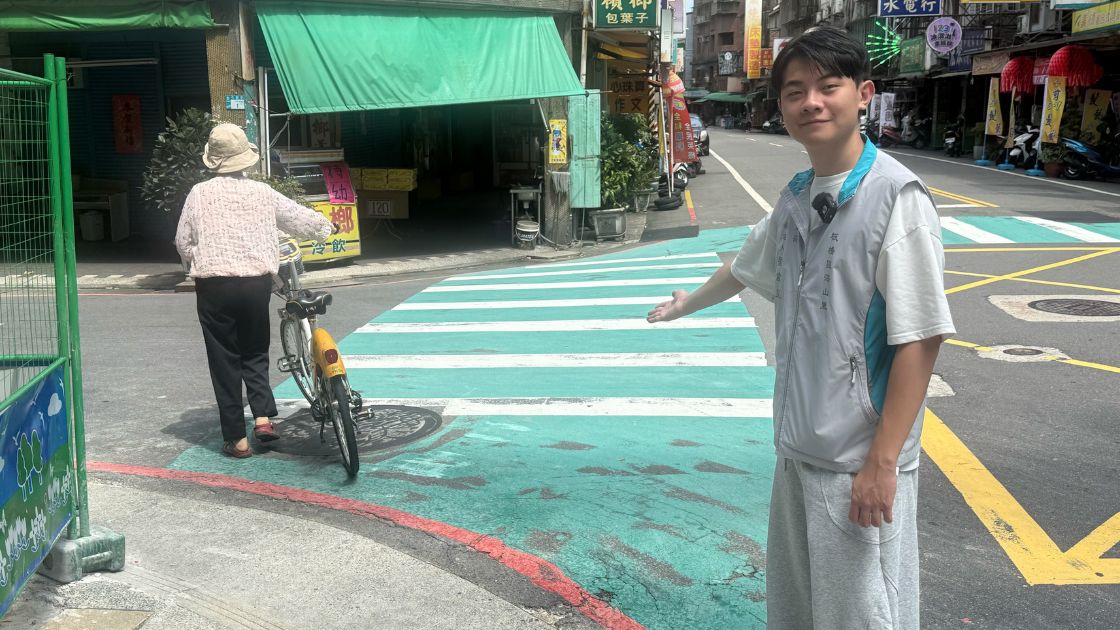 劉韋呈站在板橋海山里長安街138巷路口,伸手指向學生通行的斑馬線轉角